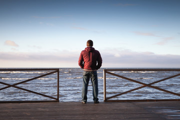 Young man looking on the sea from wooden pier