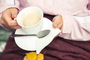Fototapeta na wymiar White cup full of coffee with cream in female hands