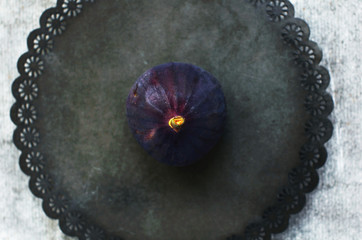 Single purple fig on rustic metal plate, top view