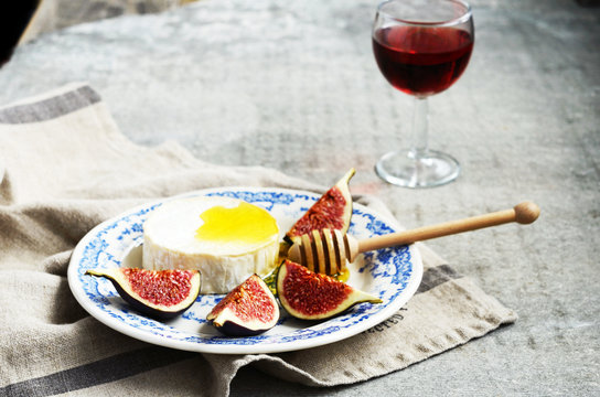 Plate with brie cheese, honey and figs and glass of wine