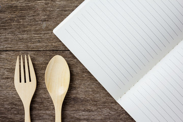 open blank lined notebook. Wooden spoon and forkon