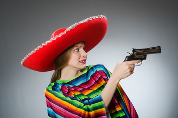 Girl in mexican vivid poncho holding handgun against gray