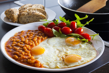 breakfast with fried eggs, beans, aragula, tomato and bread in kitchen