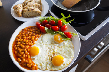 breakfast with fried eggs, beans, aragula, tomato and bread in kitchen