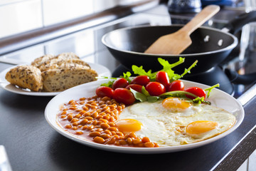 breakfast with fried eggs, beans, aragula, tomato and bread in kitchen