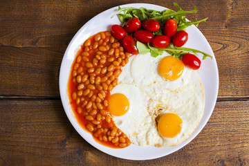 breakfast with fried eggs, beans, aragula and tomato, top view on wooden board