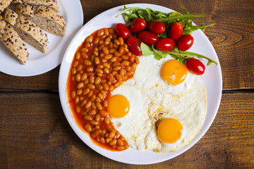 breakfast with fried eggs, beans, aragula tomato and bread, top view on wooden board