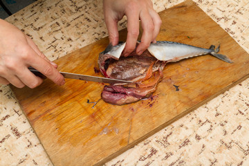 A woman chef slices a fish mackrel on a wooden Board