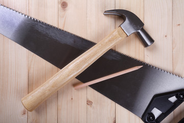 handsaw, claw hammer and pencil on wooden desk background.