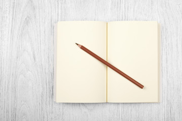 Open brown notebook and a pencil on white wooden table, top view