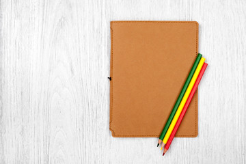 brown notebook and color pencils on white wooden table, top view