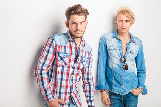 Two Young Fashion Men Standing Against Studio Wall