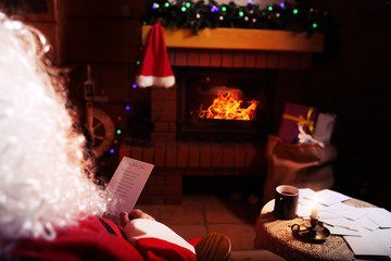Santa Claus reads letters from children in their winter cabin - obrazy, fototapety, plakaty