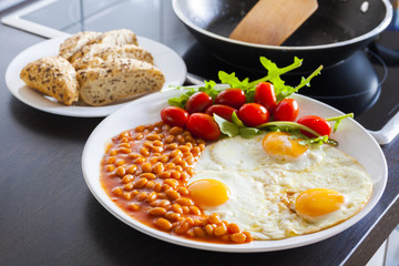 breakfast with fried eggs, beans, aragula, tomato and bread in kitchen