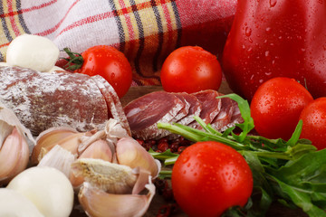 Salami with cherry tomatoes, ruccola and garlic on a cutting boa
