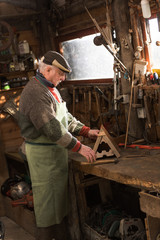 A grandfather is working on a wooden birdhouse in his workshop.