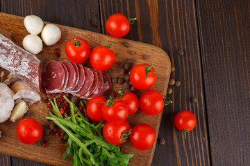 Fototapeta na wymiar Salami with cherry tomatoes, ruccola and garlic on a cutting boa