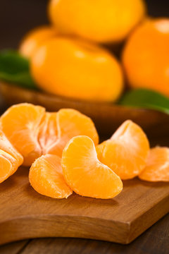 Mandarin segments on wooden board with mandarins in the back (Selective Focus, Focus on the front of the first mandarin segment)