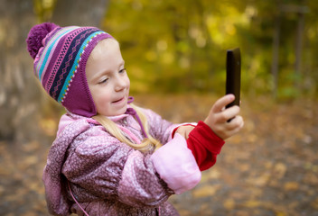 Little girl making photo or video with smartphone in the forest. Selective focus with shallow depth of field.