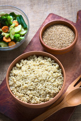 Cooked white quinoa seeds in bowl with sesame and fried vegetables in the back photographed with natural light (Selective Focus, Focus on the quinoa)