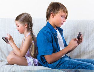 Siblings playing with smartphones on sofa