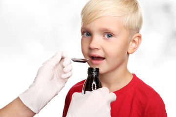 Pyszny syrop, chłopiec pije lekarstwo na przeziębienie.Dziecko przyjmuje lekarstwo podawane na łyżeczce.