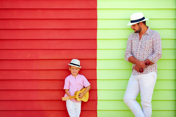 happy father and son with musical instruments near the colorful wall