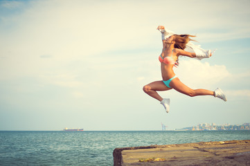 Amazing dancer in swimwear jumping up high on beach