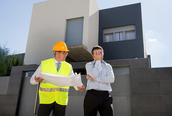 unhappy customer in stress and constructor foreman worker with helmet and vest arguing outdoors on new house building blueprints