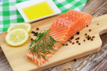 Raw salmon steak on wooden board with lemon, pepper and olive oil
