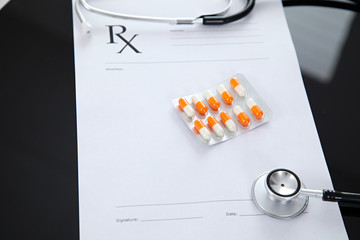 Stethoscope and prescription and pills, black reflective background