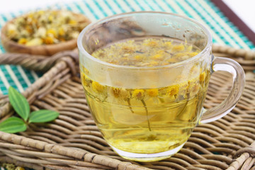 Chamomile tea in transparent glass on wicker tray
