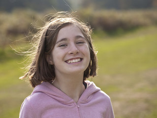 I'm Happy. A young smiling girl, eleven years old, is back lit by the sun showing up her fly away hair from running around the park.