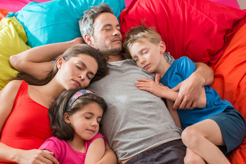 A family is taking a nap all together in a colorful bed 