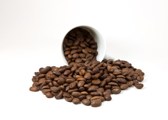 Overturned cup with coffee beans on white background