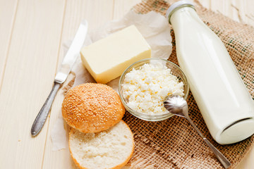 
A light breakfast of milk products , cottage cheese, sour cream and milk, roll and butter on a wooden background