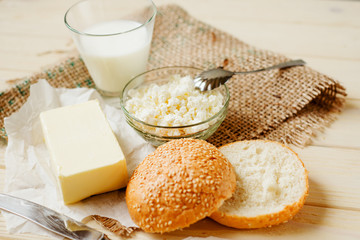 
A light breakfast of milk products , cottage cheese, sour cream and milk, roll and butter on a wooden background