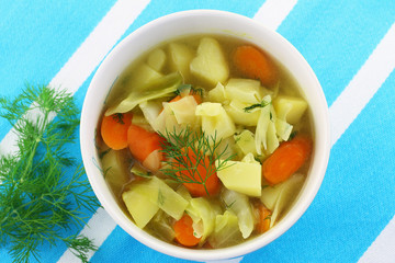 Bowl of cabbage soup with fresh dill on stripy kitchen cloth
