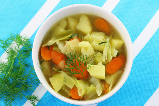 Bowl of cabbage soup with fresh dill on stripy kitchen cloth
