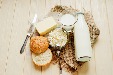 
A light breakfast of milk products , cottage cheese, sour cream and milk, roll and butter on a wooden background