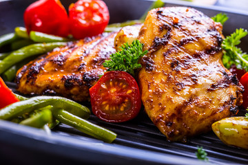 Grilled chicken breast in different variations with cherry tomatoes, green French beans, garlic, herbs, cut lemon on a wooden board or teflon pan. Traditional cuisine. Grill kitchen. 
