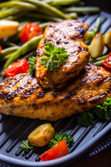 Grilled chicken breast in different variations with cherry tomatoes, green French beans, garlic, herbs, cut lemon on a wooden board or teflon pan. Traditional cuisine. Grill kitchen. 