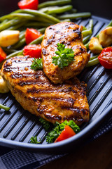 Grilled chicken breast in different variations with cherry tomatoes, green French beans, garlic, herbs, cut lemon on a wooden board or teflon pan. Traditional cuisine. Grill kitchen. 