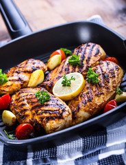 Grilled chicken breast in different variations with cherry tomatoes, green French beans, garlic, herbs, cut lemon on a wooden board or teflon pan. Traditional cuisine. Grill kitchen. 