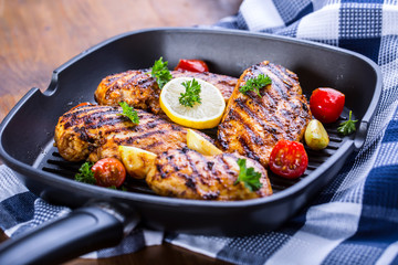 Grilled chicken breast in different variations with cherry tomatoes, green French beans, garlic, herbs, cut lemon on a wooden board or teflon pan. Traditional cuisine. Grill kitchen. 