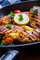 Grilled chicken breast in different variations with cherry tomatoes, green French beans, garlic, herbs, cut lemon on a wooden board or teflon pan. Traditional cuisine. Grill kitchen. 