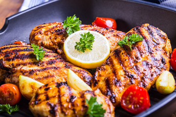Grilled chicken breast in different variations with cherry tomatoes, green French beans, garlic, herbs, cut lemon on a wooden board or teflon pan. Traditional cuisine. Grill kitchen. 