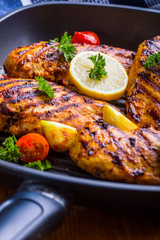 Grilled chicken breast in different variations with cherry tomatoes, green French beans, garlic, herbs, cut lemon on a wooden board or teflon pan. Traditional cuisine. Grill kitchen. 