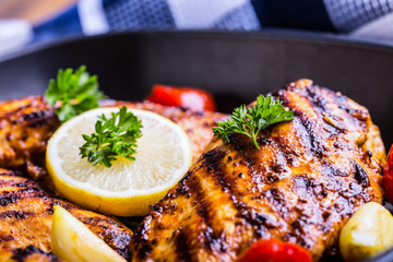 Grilled chicken breast in different variations with cherry tomatoes, green French beans, garlic, herbs, cut lemon on a wooden board or teflon pan. Traditional cuisine. Grill kitchen. 