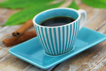 Black coffee in vintage stripy cup and cinnamon sticks on rustic wooden surface
